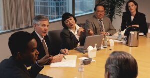 Business professionals seated around a conference table during a formal meeting or policy discussion.