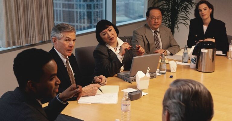 Business professionals seated around a conference table during a formal meeting or policy discussion.
