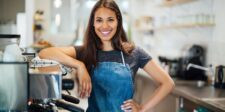 What to know before getting a business insurance quote Smiling café worker in an apron standing beside an espresso machine in a bright coffee shop.