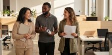 Three professionals walking through a bright modern office while talking and carrying documents.