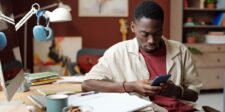How to get good at anything: 5 steps to learn faster and improve for real Young man sitting at a desk and looking at his phone in a creative home office.