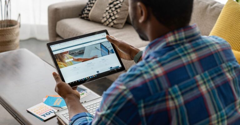 Person using a tablet to view LinkedIn while sitting at home with a laptop nearby.