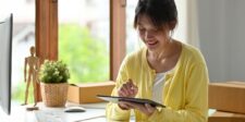 The obsessive learner's guide to building a one-person business Woman using a tablet at a home office desk with moving boxes nearby, representing someone starting or managing a one-person business.