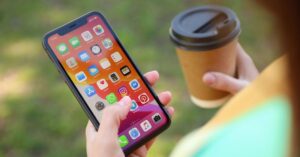 A person holds an iPhone in one hand and a takeaway coffee cup in the other while using smartphone apps outdoors.