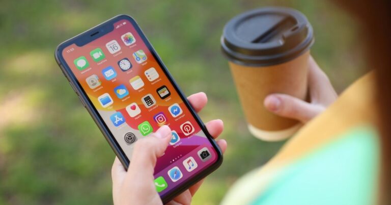 A person holds an iPhone in one hand and a takeaway coffee cup in the other while using smartphone apps outdoors.