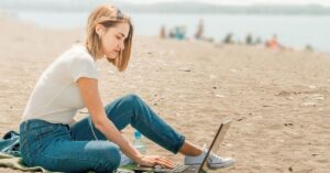 Person sitting on a beach and working on a laptop.