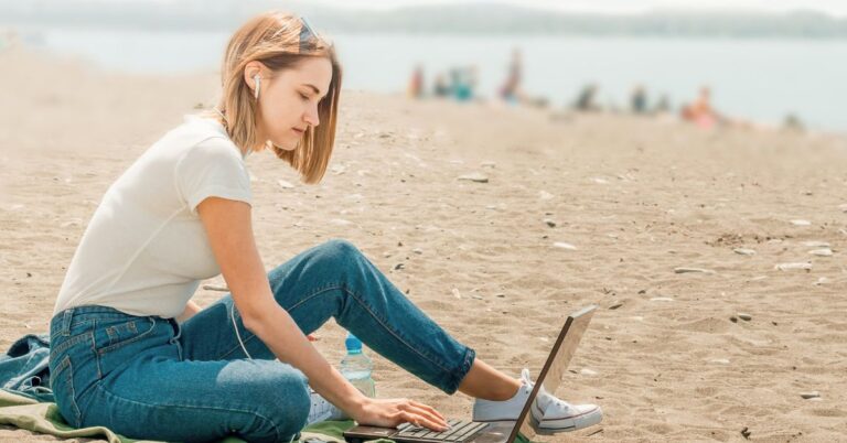 Person sitting on a beach and working on a laptop.