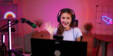 YouTube's AI detector is live and it doesn't need your permission A smiling video creator wearing headphones waves at the camera while recording in a colorful home studio.
