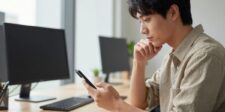 68% of Google searches now end without a click, new research shows Man sitting at a desk and looking at his smartphone beside two computer monitors.