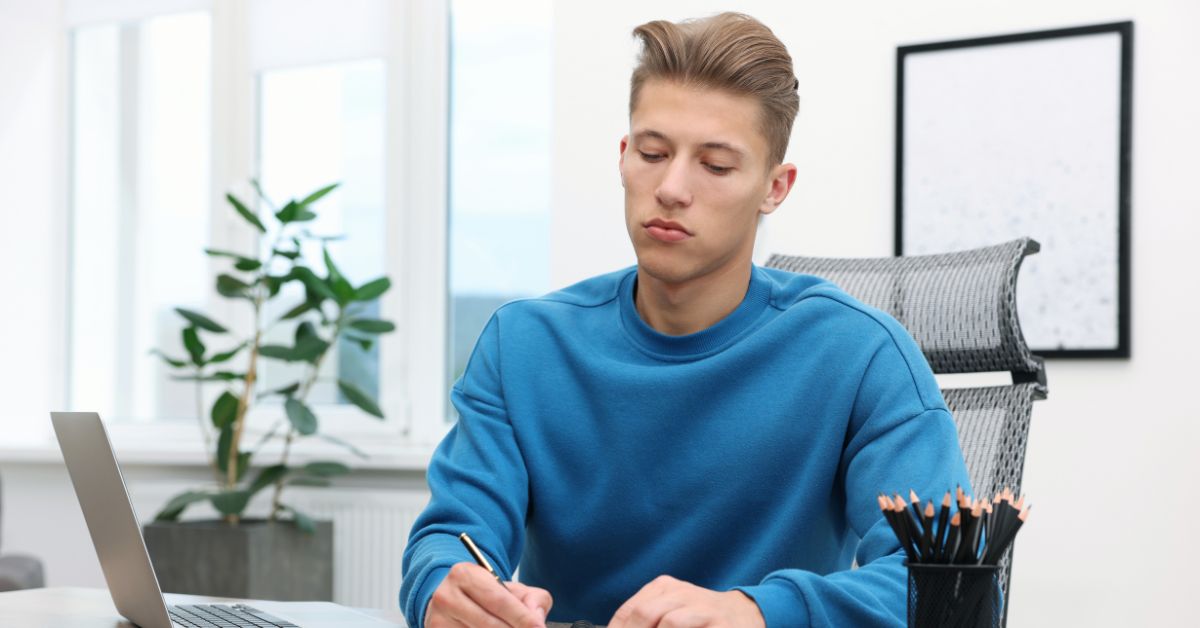 Young ad copywriter at a desk beside a laptop and a cup of pencils in a bright office.