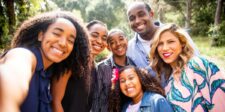 Smiling family posing together for an outdoor selfie in a sunny park.