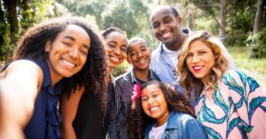 Smiling family posing together for an outdoor selfie in a sunny park.