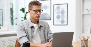 Man wearing glasses and working on a laptop at a desk.
