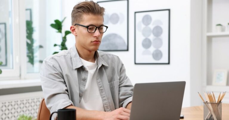 Man wearing glasses and working on a laptop at a desk.