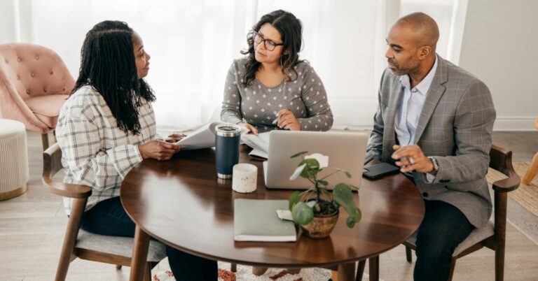 Three people sitting around a table with a laptop and documents during a business meeting.