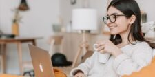 How to make money with digital marketing: practical paths that hold up Smiling woman wearing glasses and holding a mug while using a laptop at home.