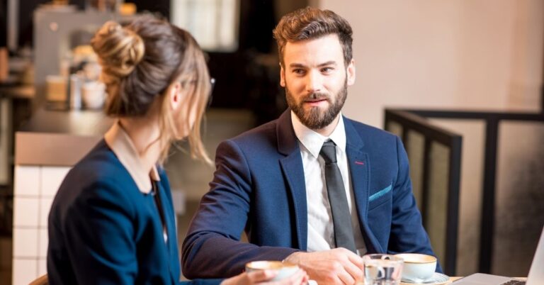 Man and woman in business attire having a conversation at a table with coffee.