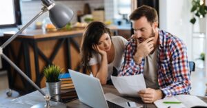 Concerned couple sitting at a table and reviewing documents beside a laptop.