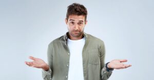 Man in a green shirt shrugging against a light gray background.