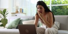 Worried woman sitting on a couch and looking at a laptop.