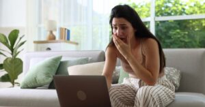 Worried woman sitting on a couch and looking at a laptop.