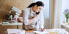 New 50% U.S. tariffs on Canadian products: how businesses should prepare Small business owner writing notes while talking on the phone in a bright workspace with baking supplies nearby.