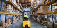 Warehouse and industrial security: what a commercial security camera installation must cover Forklift operator driving through a warehouse aisle lined with tall shelves and stacked boxes.