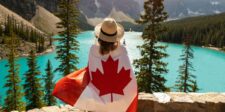 What Canada Day 2026 just told you about your business Person wrapped in a Canadian flag looking out over a bright turquoise mountain lake surrounded by trees.