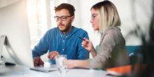 The $2.59 trillion question — why isn't AI making anyone richer? Two professionals reviewing work together at a desktop computer in a bright office.