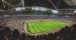 Crowded soccer stadium during a match, viewed from the stands under bright stadium lights.