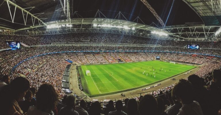 Crowded soccer stadium during a match, viewed from the stands under bright stadium lights.