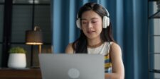 How to make money writing in 2026 Person wearing headphones working on a laptop in a dim room with blue curtains.