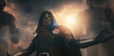 Armored masked figure standing in a dramatic smoky scene.