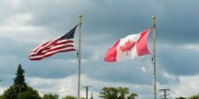 U.S. and Canadian flags flying on flagpoles beneath a cloudy sky.