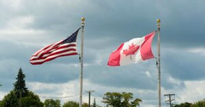 U.S. and Canadian flags flying on flagpoles beneath a cloudy sky.