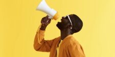 Man speaking into a megaphone against a bright yellow background.