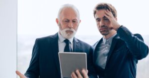 Two business professionals looking concerned while reviewing information on a tablet.