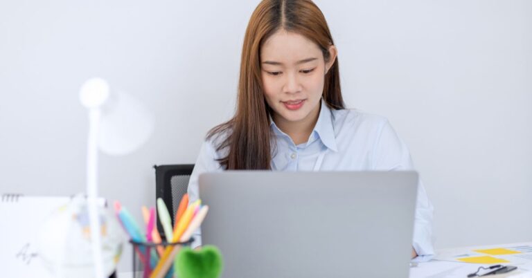 Woman working on a laptop at a desk in a bright office setting.