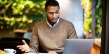 Man looking concerned while working on a laptop at a table.
