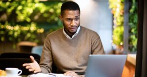 Man looking concerned while working on a laptop at a table.