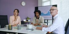GA4 just made budget reviews easier to misread Three coworkers in a meeting looking toward a presentation screen showing business performance charts.