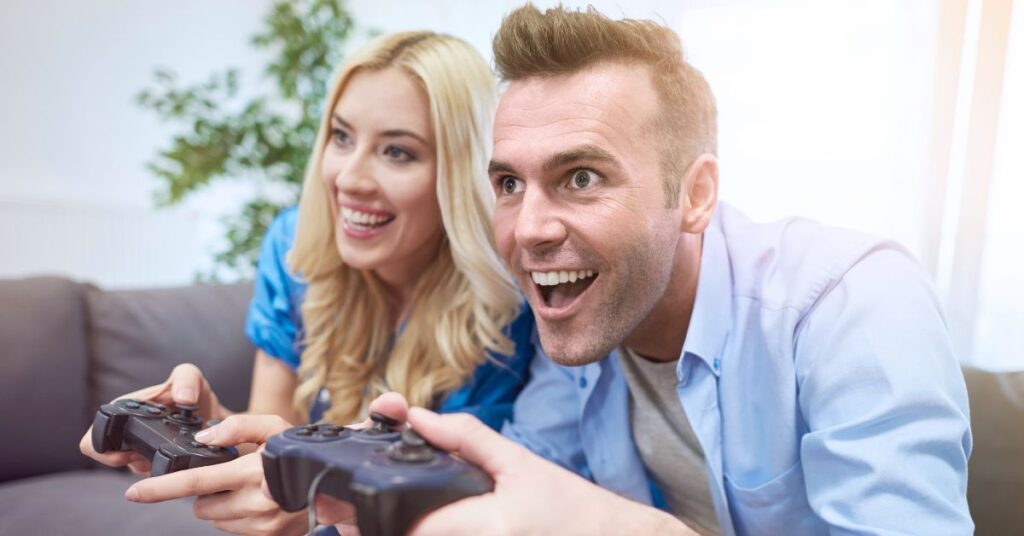 Excited man and woman playing video games together with controllers while sitting on a couch.