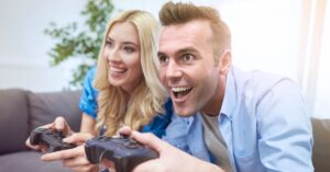 Excited man and woman playing video games together with controllers while sitting on a couch.