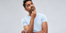 Google is moving Local Services Ads into Google Ads Man in a light blue shirt looking up with one hand on his chin against a gray background.