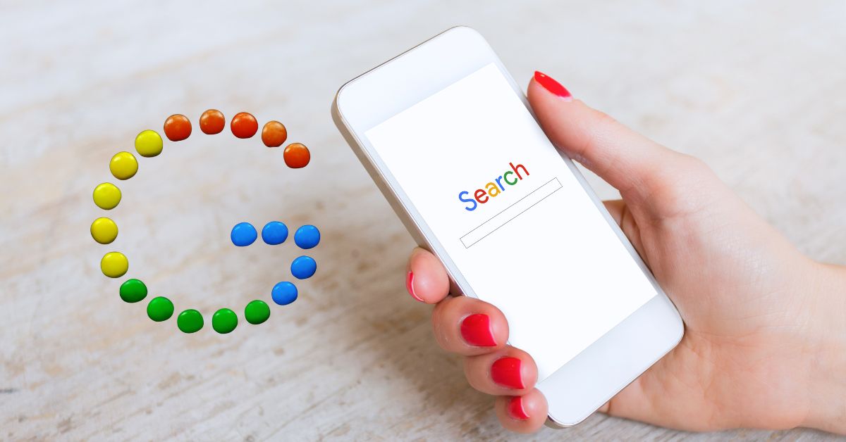 Hand holding a smartphone displaying a search page beside a stylized multicoloured Google “G.”