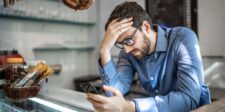 Google's August 2026 spam update is still rolling out Concerned man in glasses looking at his smartphone while leaning on a counter.