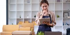 Google's Content API for Shopping is retired: what to do if you missed the August 18 deadline Small business owner reviewing a clipboard beside shipping boxes and a laptop in a workspace.