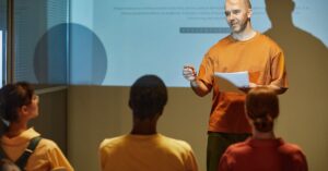 A man giving a presentation to a seated audience in a classroom or workshop setting.