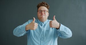 Man in glasses giving two thumbs up against a dark background.