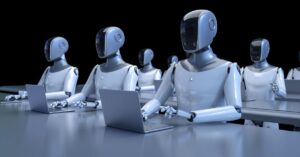 Humanoid robots seated at desks using laptops in a dark workspace.